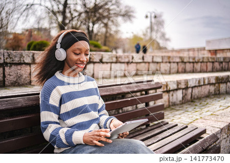 Young woman enjoying music streaming on digital tablet in park Young woman enjoying music streaming on digital tablet in park 141773470