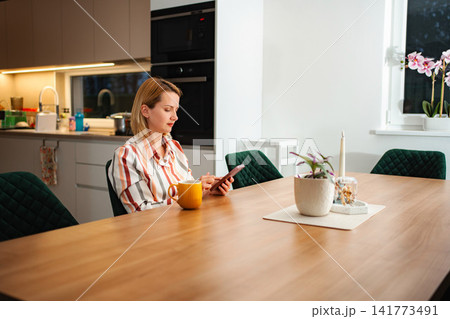 Woman using smartphone at modern kitchen dining table Woman using smartphone at modern kitchen dining table 141773491