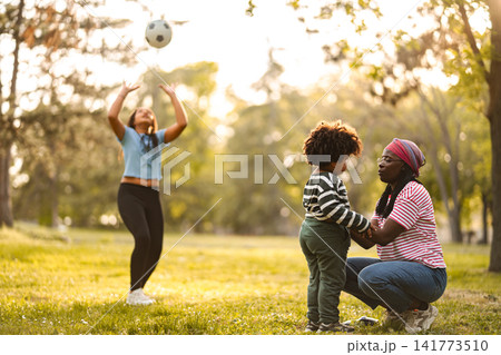 Mother and daugther playing football with child watching in park 141773510