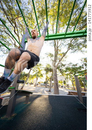 Person exercises on outdoor gym equipment during bright day in park Person exercises on outdoor gym equipment during bright day in park 141773912