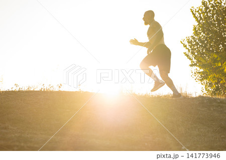 Man running up a hill during sunrise with bright light shining behind him Man running up a hill during sunrise with bright light shining behind him 141773946