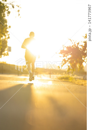 Sunrise runner on a path surrounded by trees in a park 141773967