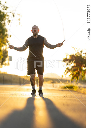 Man skips rope in the sunlight on a road, enjoying the activity during the early morning hours 141773971