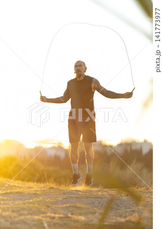 Person jumps rope during sunset in an outdoor setting with a warm glow in the background Person jumps rope during sunset in an outdoor setting with a warm glow in the background 141773977