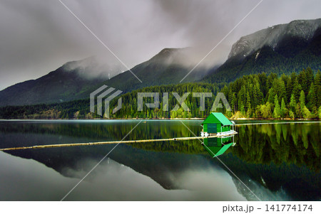 Misty Mountain Lake with Forest Reflection and Green Boathouse Misty Mountain Lake with Forest Reflection and Green Boathouse 141774174