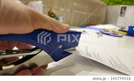 Close-Up of a Hand Using a Blue Stapler on Documents Close-Up of a Hand Using a Blue Stapler on Documents 141774318