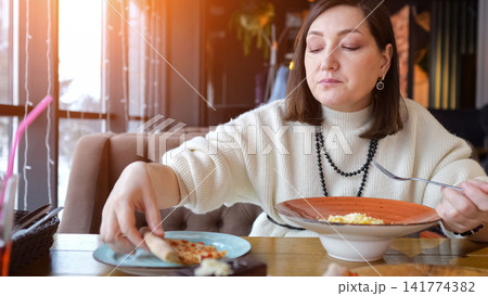 Woman Reaching For Soup At Cafe, Spoon Poised Over Steaming Bowl With Attentive Expression Editor Warming Up With Nourishing Broth Between Afternoon Meetings In Relaxed Interior. 141774382