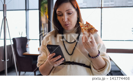 Woman Entertains While Eating Lunch. Female Professional Responds To Messages While Enjoying Pizza And Working. Woman Balances Her Smartphone Response Duties And Pizza Snack During Brief Cafe Break 141774408