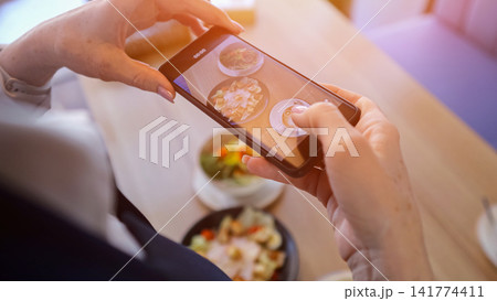 Elderly Woman Photographs. Businesswoman Captures Food Moments. Senior Lady Takes Pictures Of Meal. Mature Businesswoman Records Images Of Delicious Dish Using Her Smartphone For Online Sharing Elderly Woman Photographs. Businesswoman Captures Food Moments. Senior Lady Takes Pictures Of Meal. Mature Businesswoman Records Images Of Delicious Dish Using Her Smartphone For Online Sharing 141774411