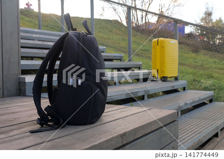 Travel Items Positioned On Stairs Against Grassy Landscape Background. Scene Depicting Travel Essentials Including Backpack And Suitcase On Outdoor Stairs With Natural Surroundings Travel Items Positioned On Stairs Against Grassy Landscape Background. Scene Depicting Travel Essentials Including Backpack And Suitcase On Outdoor Stairs With Natural Surroundings 141774449