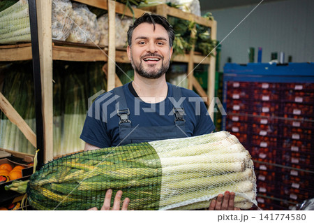 Smiling man handling fresh leeks in produce warehouse Smiling man handling fresh leeks in produce warehouse 141774580