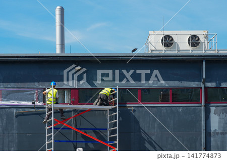 Construction Workers Installing Exterior Window Film from Mobile Scaffold on Commercial Building Facade 141774873