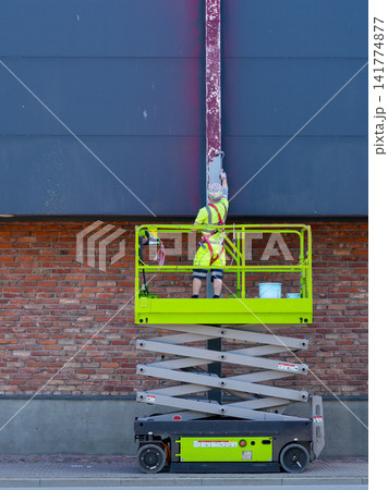 Construction Worker Painting Steel Column from Scissor Lift at Commercial Building Exterior Facade 141774877