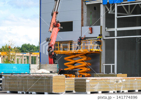 Industrial Sandwich Panel Wall Installation Using Scissor Lift and Crane at Modern Construction Site Industrial Sandwich Panel Wall Installation Using Scissor Lift and Crane at Modern Construction Site 141774896