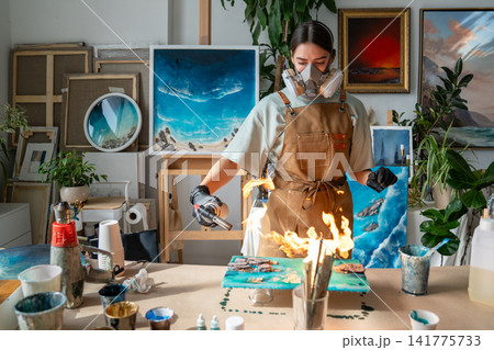 Woman crafter in respirator using professional tools and creating liquid art using epoxy resin. Woman crafter in respirator using professional tools and creating liquid art using epoxy resin. 141775733