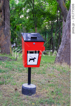 Bright Dog Waste Bin in Public Park. Red dog waste disposal bin with pet pictogram stands among trees and grass in public park. Urban cleanliness, responsible pet ownership infrastructure 141775806