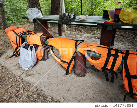 Bright orange life jackets arranged on wooden picnic bench 141775881