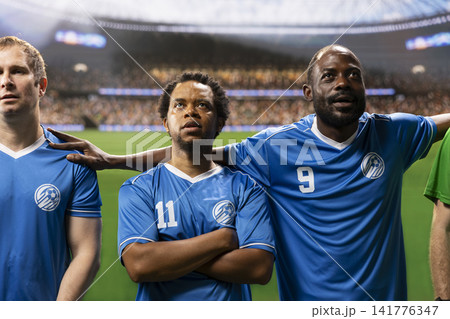 Diverse soccer players stand together during pre-match anthem ceremony, teammates and goalkeeper in lineup before football game on pitch. Blurred stadium crowd in arena. Diverse soccer players stand together during pre-match anthem ceremony, teammates and goalkeeper in lineup before football game on pitch. Blurred stadium crowd in arena. 141776347