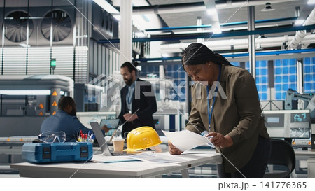 African american female expert reviewing solar panels production line, doing quality control in a photovoltaics factory. Analyzing data reports and insight to create solar power. Camera A. African american female expert reviewing solar panels production line, doing quality control in a photovoltaics factory. Analyzing data reports and insight to create solar power. Camera A. 141776365