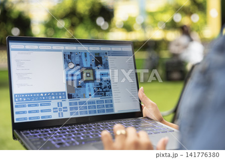 Close up of woman using software with microchip and circuit board interface on laptop in city park, illustrating semiconductor engineering and hardware monitoring. Close up of woman using software with microchip and circuit board interface on laptop in city park, illustrating semiconductor engineering and hardware monitoring. 141776380