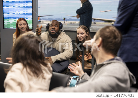 Chatting, diversity and group of friends inside busy airport lounge. Doing conversation, long flight layover and multiethnic passengers sitting on chairs in transit hub before departure Chatting, diversity and group of friends inside busy airport lounge. Doing conversation, long flight layover and multiethnic passengers sitting on chairs in transit hub before departure 141776433