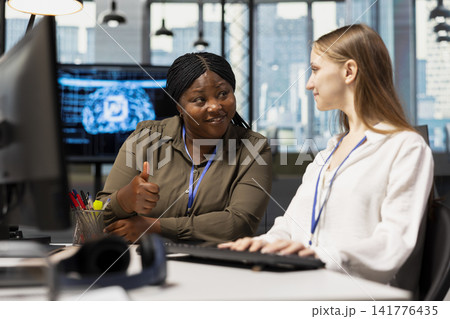 Cheerful IT specialist teaching intern to use artificial intelligence. African american woman guiding junior dev through AI tool integration, mentoring her on using machine learning APIs 141776435