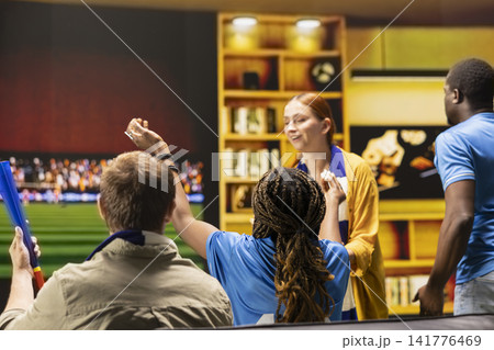 Close up of football supporters on couch following match on TV screen. Home watch party guests enjoying live game television broadcast on soccer stadium 141776469