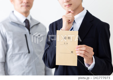 給料袋を持って悩むリクルートスーツを着た若い男性と作業服のミドル男性 給料袋を持って悩むリクルートスーツを着た若い男性と作業服のミドル男性 141777073