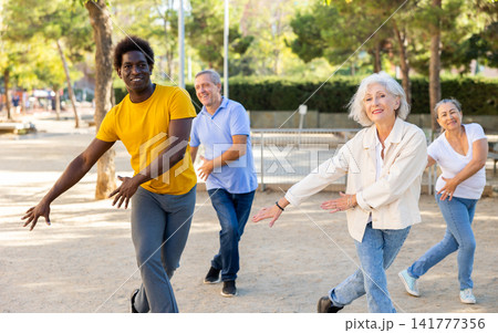 Positive multiracial mature casual pensioners practicing group dancing outdoors in autumn Positive multiracial mature casual pensioners practicing group dancing outdoors in autumn 141777356