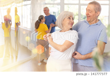 Elderly man in dance hall with female partner and dances Latin rumba. Hobby, healthy lifestyle concept Elderly man in dance hall with female partner and dances Latin rumba. Hobby, healthy lifestyle concept 141777377