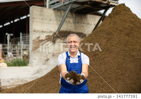Elderly man holding handful of manure Elderly man holding handful of manure 141777391