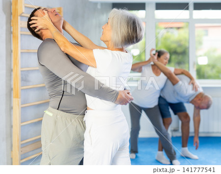 Senior woman in pair with middle-aged coach train Krav Maga and self-defense skills. Senior woman in pair with middle-aged coach train Krav Maga and self-defense skills. 141777541