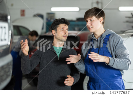 Young man car mechanic talks with man client in workshop and takes order. 141777627