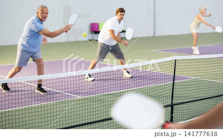 Elderly man playing pickleball in team with male partner indoors Elderly man playing pickleball in team with male partner indoors 141777638