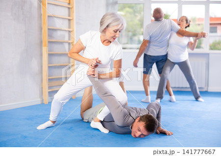 Senior woman in pair with middle-aged coach train Krav Maga and self-defense skills. Senior woman in pair with middle-aged coach train Krav Maga and self-defense skills. 141777667
