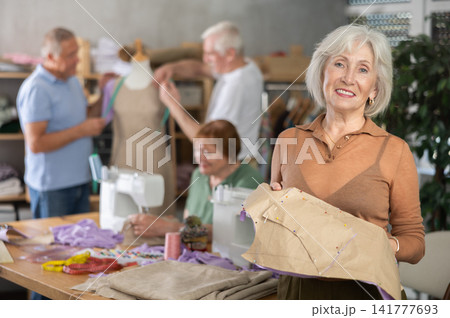 Elderly woman demonstrating paper pattern in training sewing workshop 141777693