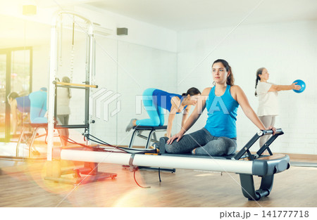 Young girl practicing pilates stretching exercises on reformer Young girl practicing pilates stretching exercises on reformer 141777718