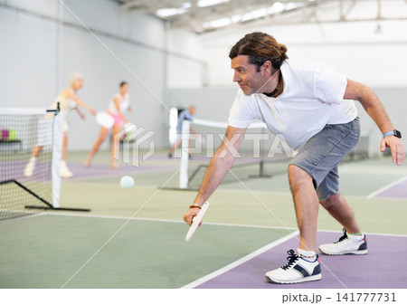 Athletic man and partner playing pickleball tennis on the pickleball court indoors 141777731