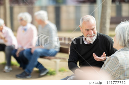 Elderly couple flirting while sitting on bench in courtyard 141777732