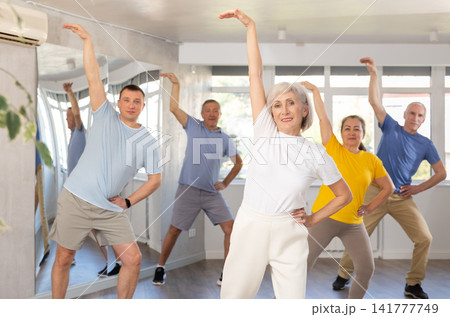 Elderly woman practicing Tai Chi with group in training room Elderly woman practicing Tai Chi with group in training room 141777749