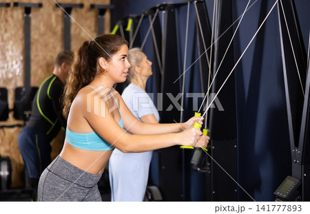 Athletic woman training her arms on simulator with ropes Athletic woman training her arms on simulator with ropes 141777893