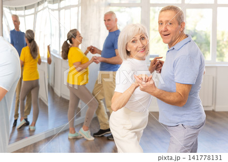 Group of happy mature pensioners learning to dance latin dances in dance studio Group of happy mature pensioners learning to dance latin dances in dance studio 141778131