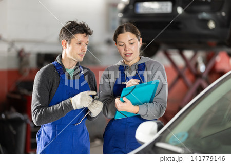 Young woman supervisor manager of car repair station with papers listens to male master Young woman supervisor manager of car repair station with papers listens to male master 141779146