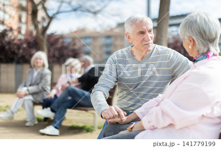 Elderly couple sitting on bench, flirting, chatting Elderly couple sitting on bench, flirting, chatting 141779199