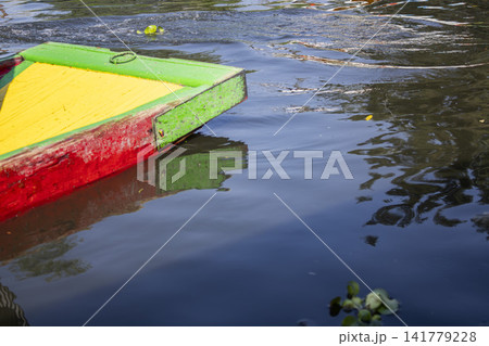 Xochimilco colorful wooden trajinera floating on calm water with reflections Xochimilco colorful wooden trajinera floating on calm water with reflections 141779228