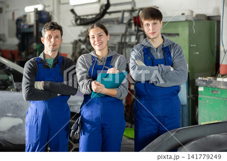 Team of auto mechanics, two men and one woman, wearing blue overalls and posing, ready to provide professional vehicle service Team of auto mechanics, two men and one woman, wearing blue overalls and posing, ready to provide professional vehicle service 141779249
