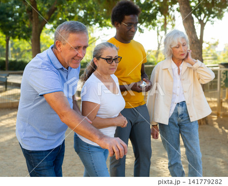 A group of multiracial mature adult people playing patanque game outdoors in a park A group of multiracial mature adult people playing patanque game outdoors in a park 141779282