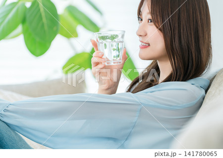 リビングのソファに座り水,白湯を飲む若いアジア人女性 リビングのソファに座り水,白湯を飲む若いアジア人女性 141780065