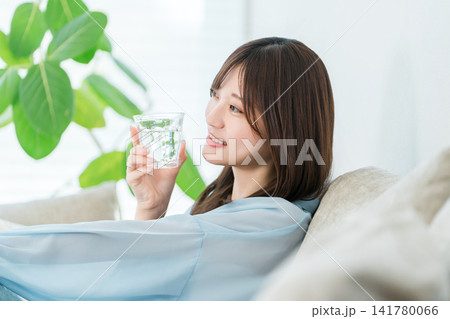 リビングのソファに座り水,白湯を飲む若いアジア人女性 リビングのソファに座り水,白湯を飲む若いアジア人女性 141780066