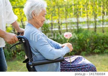 Asian senior or elderly old lady woman holding red rose flower, smile and happy in the sunny garden. 141780084